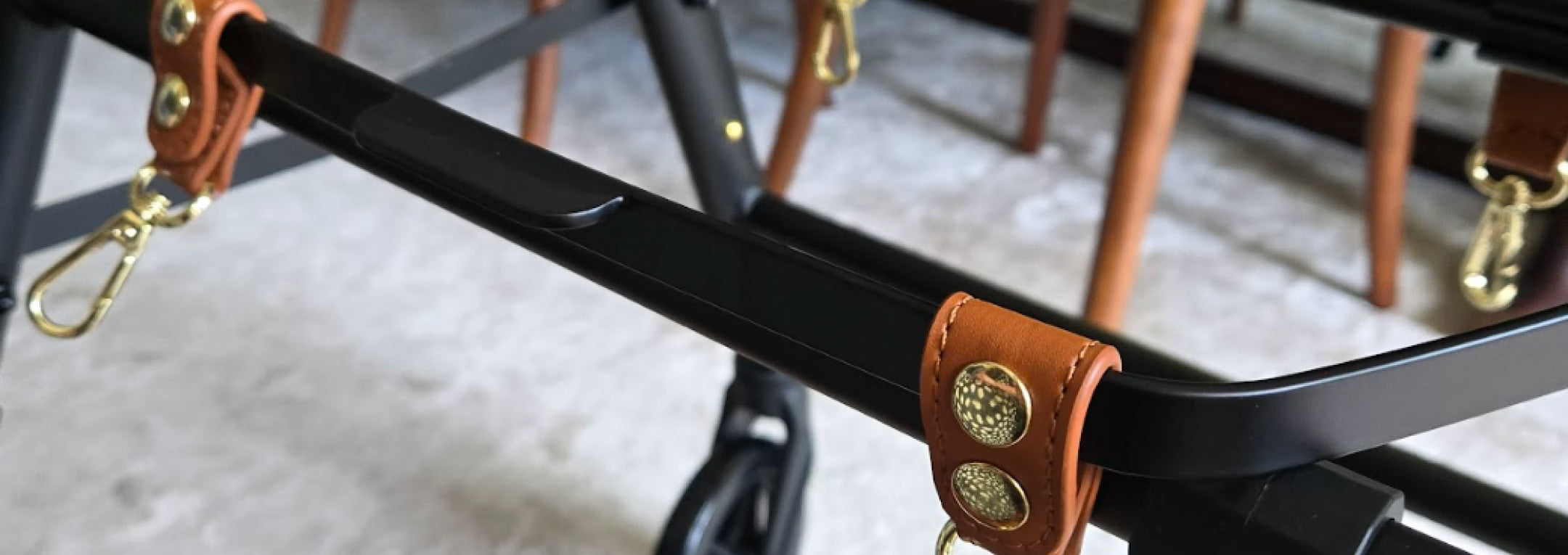 Close-up of a black metal frame with brown leather straps and gold hardware on a blurred background.